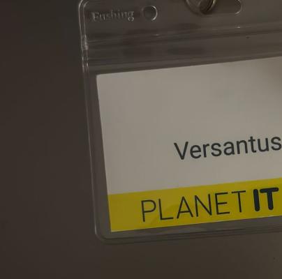 A close-up of a Versantus corporate name badge on a yellow Planet IT lanyard at an IT networking event.